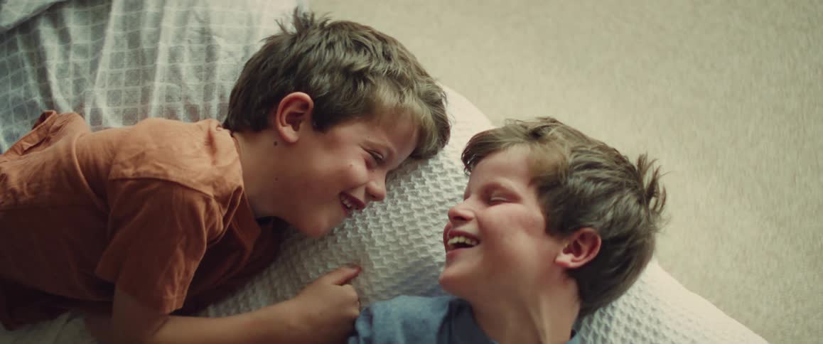 A heartwarming slow-motion shot captures two young brothers laughing and playfully tickling each other while lying on a bed