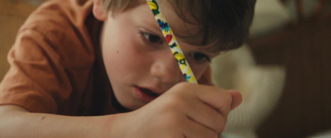 An intimate close-up shot of a young boy concentrating intently as he draws with his pencil