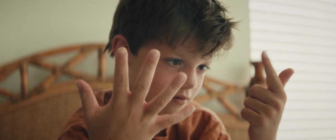 A focused young child slowly counts up to eight on his fingers while learning math