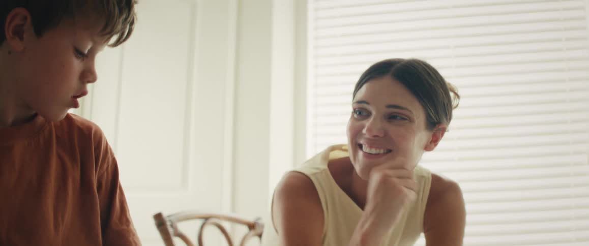 A joyful mother and her young son laugh and play together, sharing a loving and ticklish moment on a bed in a sunlit room