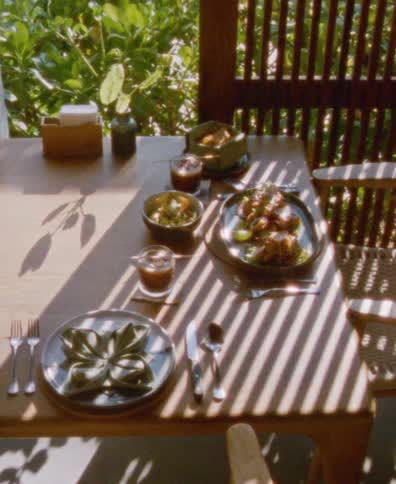 A dreamy, sunlit still life of an elegant meal for two on a wooden table surrounded by lush greenery