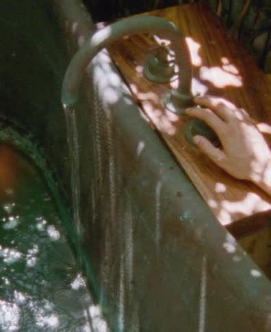 A stream of water fills a vintage outdoor bathtub as a hand rests on the faucet, captured in a serene, sun-dappled high-angle shot