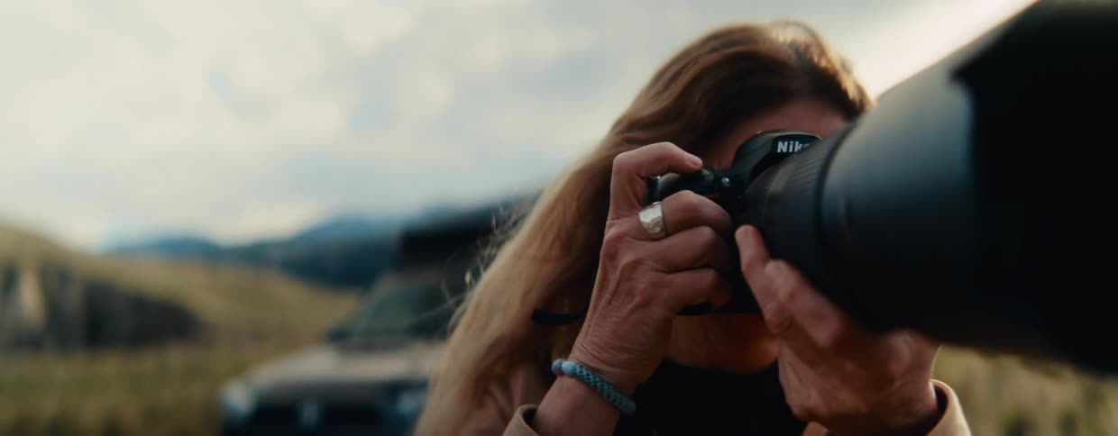 Close-up of a happy female photographer taking a picture in the wilderness, then smiling with satisfaction