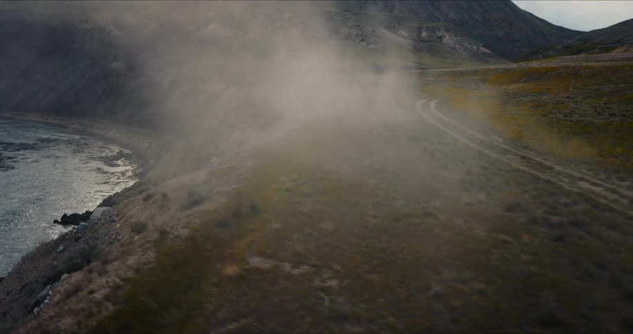 An atmospheric aerial shot pulls back through the fog to reveal a vast canyon landscape with a winding river and train tracks