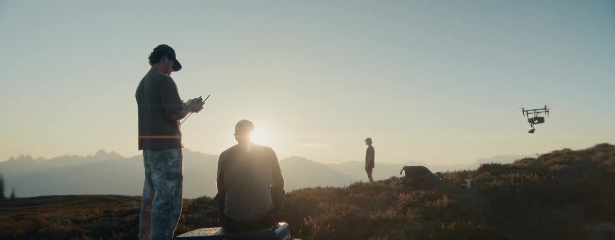 A drone pilot and his team stand on a scenic mountain overlook preparing to fly their drone at sunrise