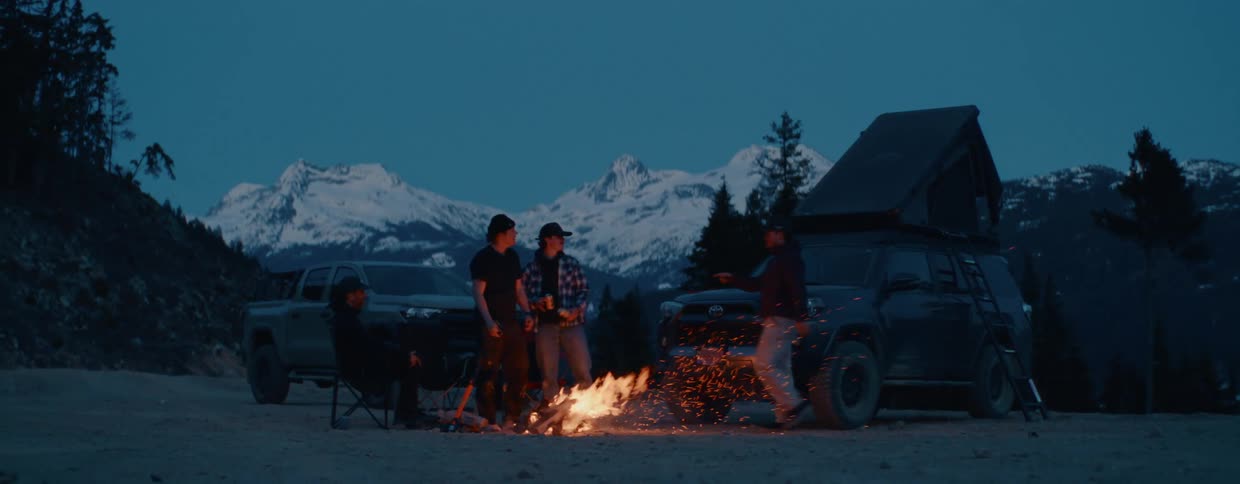 A group of friends enjoys a bonfire during an overland camping trip in the mountains at dusk