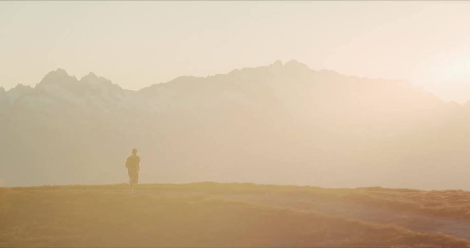 Epic slow motion shot of a man trail running along a scenic mountain path during a hazy golden hour sunrise