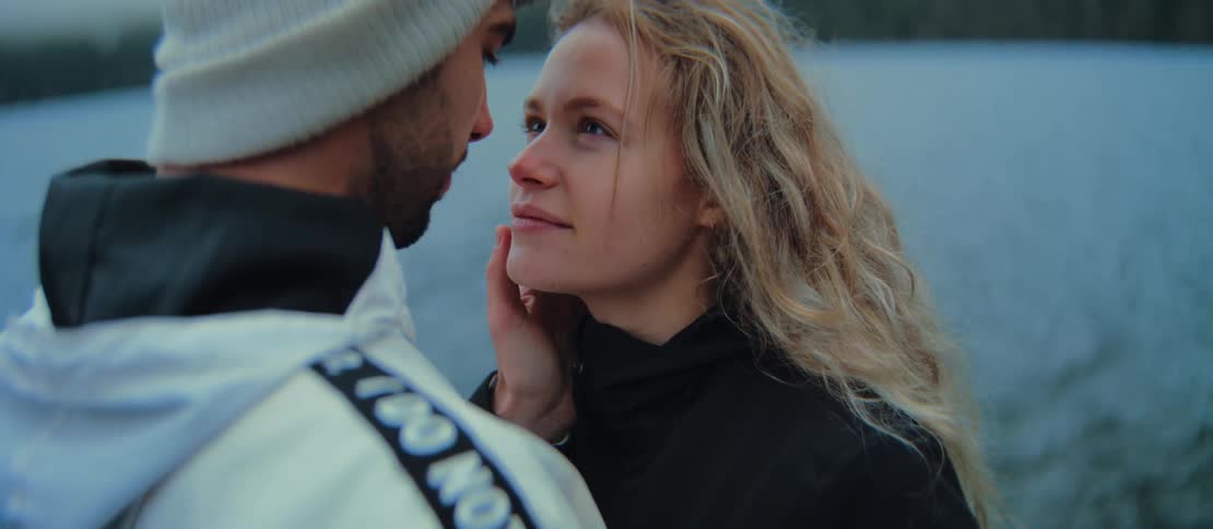 An intimate close-up of a loving couple gently touching noses by the water on a cool, overcast day