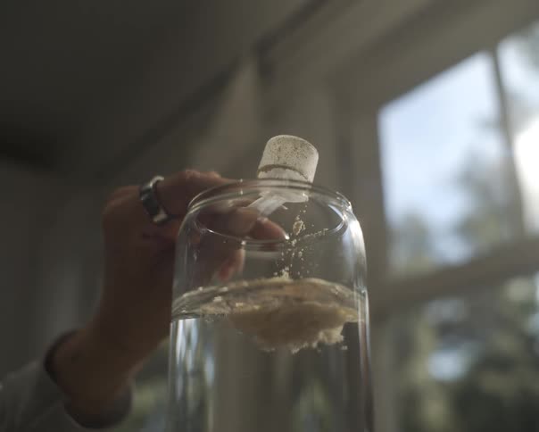 Slow motion close-up of a powdered supplement being poured from a scoop into a glass of water, dissolving as it hits the surface