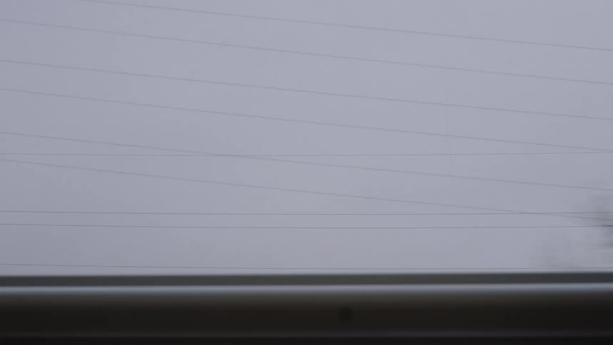 A point-of-view shot from a moving vehicle captures a blurry, grey landscape on an overcast day