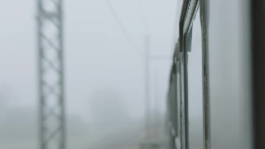 A blurry, atmospheric view from a train window looking down the side of the train as it moves through a foggy landscape