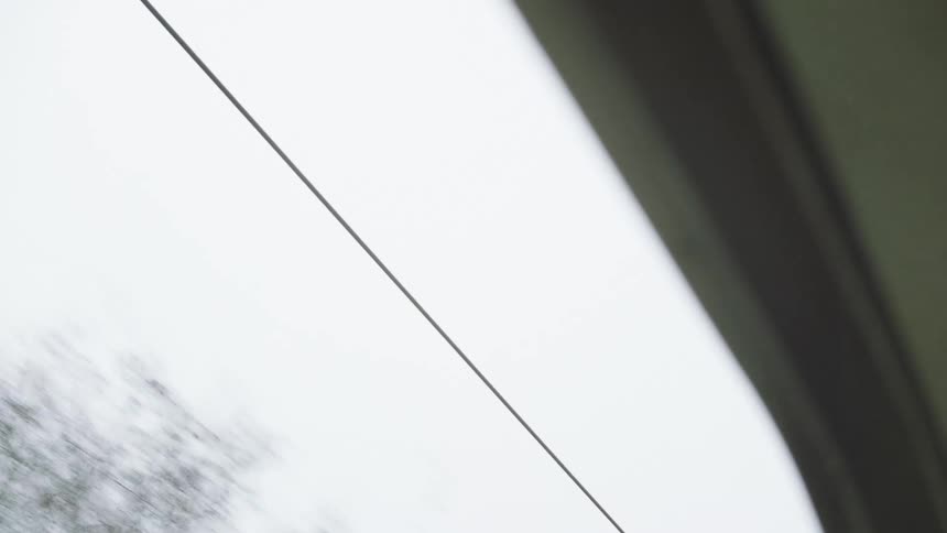 View from a moving vehicle's window of a power line against an overcast sky with blurred trees passing by