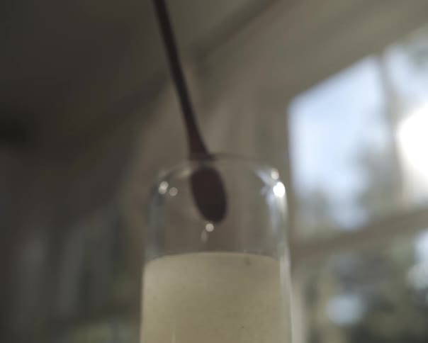 A slow-motion close-up of a spoon being lifted out of a frothy white drink with drops falling back into the glass