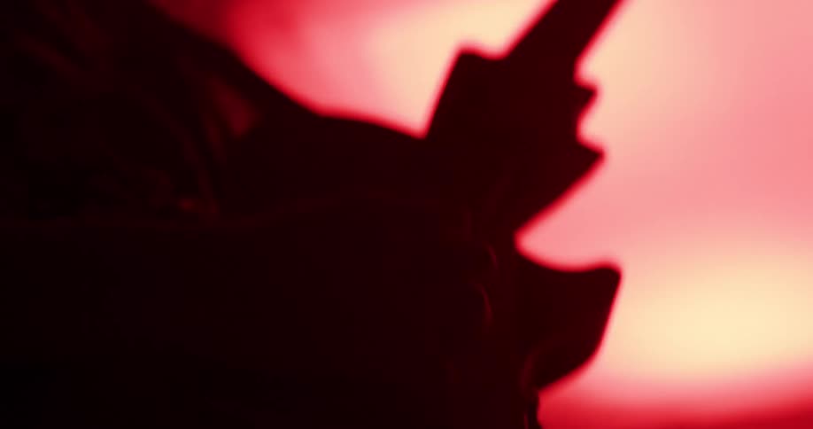 Silhouette of a guitarist passionately playing an electric guitar in a dark, red-lit room