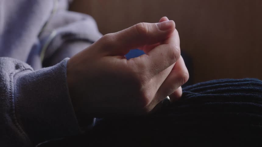 Close up of a hand resting on a knee as the fingers slowly unclench in a dimly lit setting