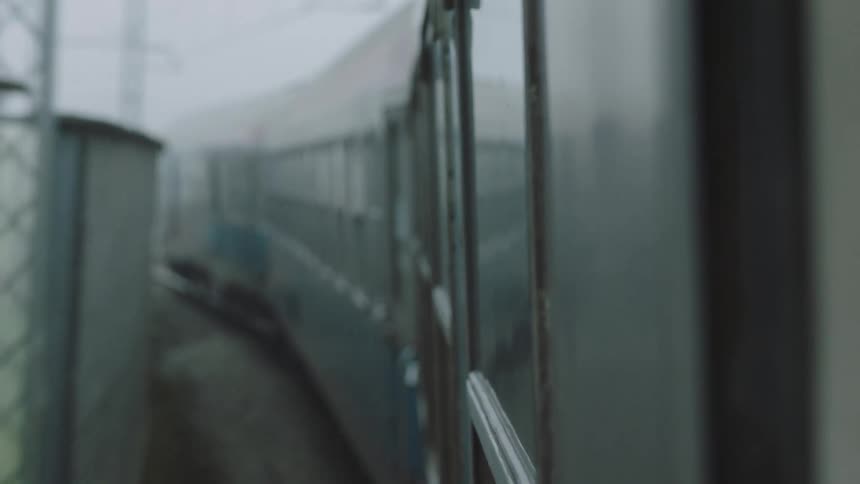 A view from a passenger train window shows the train cars moving through thick fog on a gloomy day