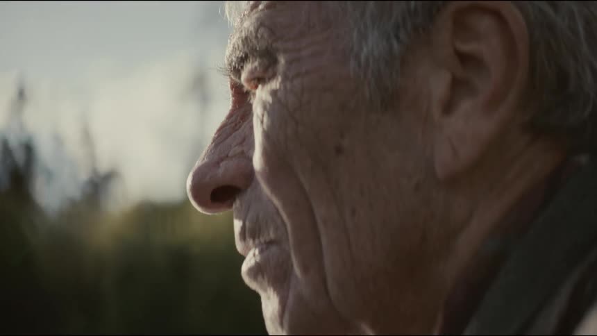 A slow-motion close-up reveals the thoughtful profile of an elderly man gazing into the warm sun