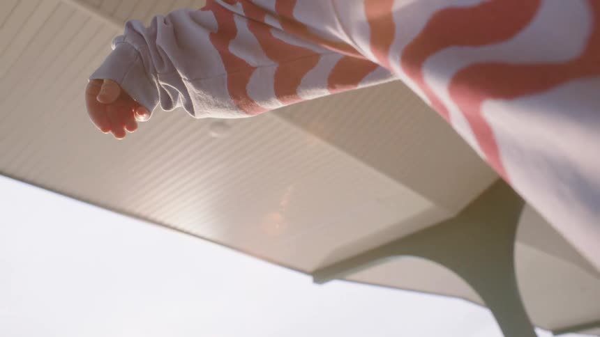 A person wearing a wavy striped sweatshirt slowly raises their arm, catching the golden hour sun flare