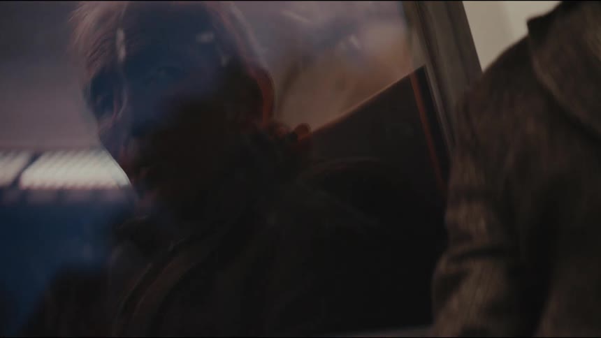 Close up of a somber elderly man's reflection in a train window as he travels through the night