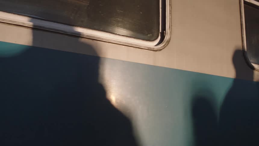 Shadows of anonymous commuters are cast on the side of a moving train car in the warm evening light