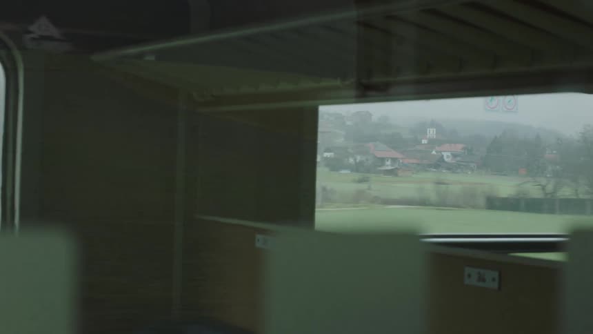 The European countryside and a small village pass by in the reflection of an empty train car window