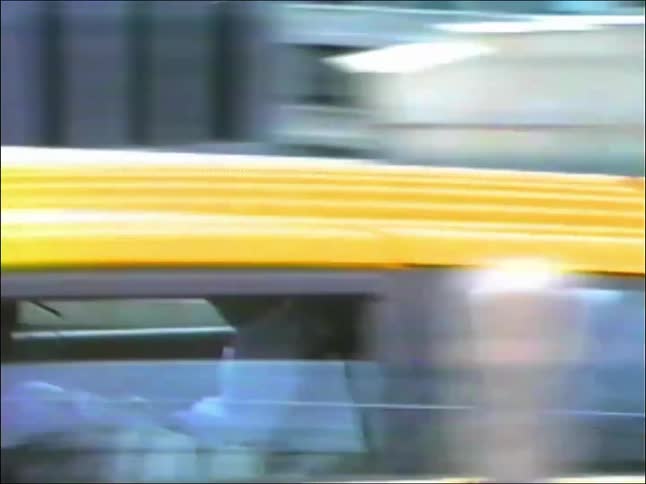 Vintage home video footage tracks a yellow taxi van as it drives across a city bridge amidst traffic