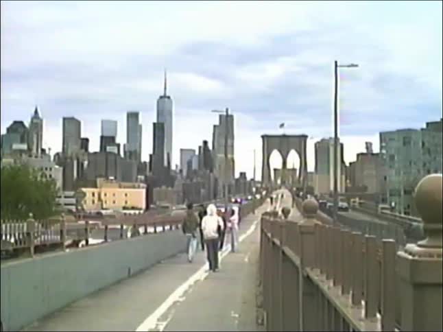 A vintage-style shot shows pedestrians walking on the Brooklyn Bridge with the modern Manhattan skyline in the background