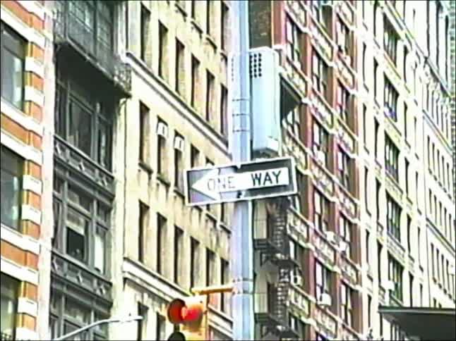 An authentic 1990s VHS clip showing a one-way street sign against a backdrop of city architecture