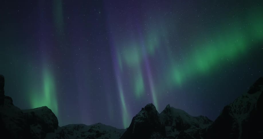 The vibrant green and purple Northern Lights illuminate the starry night sky above a mountain range