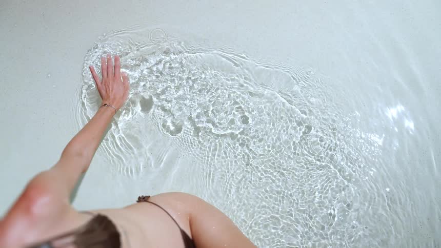 Overhead slow motion shot of a woman's hand gracefully creating ripples as it glides through clear, sunlit water
