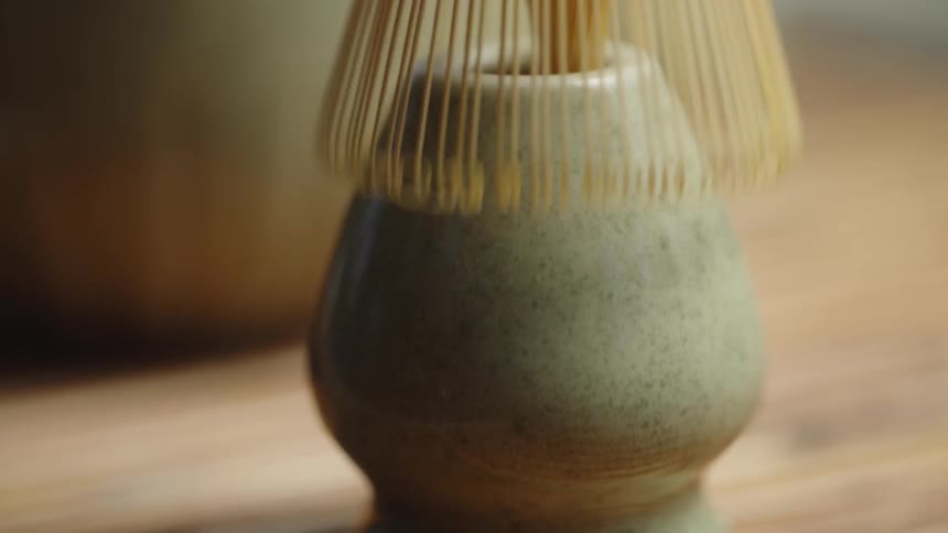 Slow-motion close-up reveals a traditional bamboo chasen whisk being lifted from its holder to prepare a matcha tea ceremony