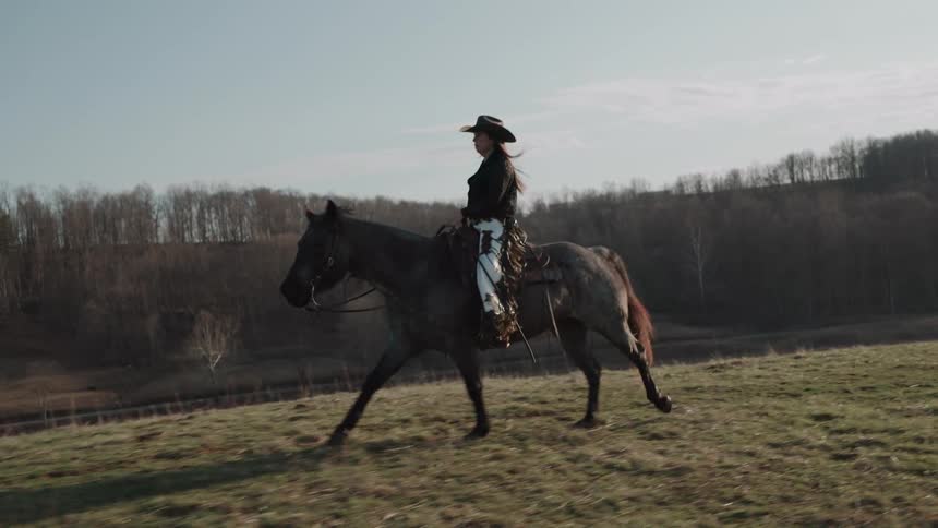 A confident cowgirl rides her majestic horse across a wide-open field in beautiful slow motion