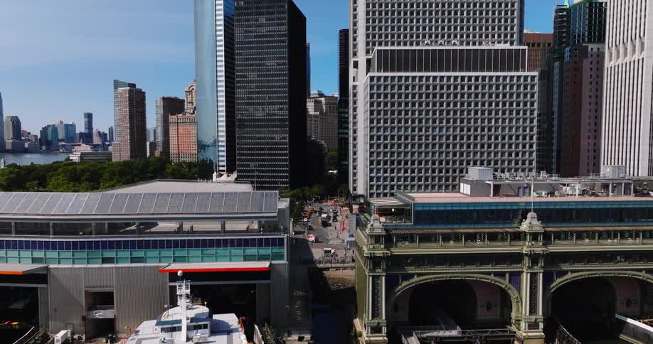 An aerial view of Lower Manhattan pulls back to show the Staten Island Ferry departing from the Whitehall Terminal on a sunny day