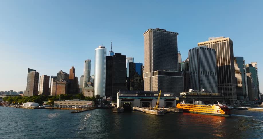 A Staten Island Ferry departs from the Whitehall Terminal in Lower Manhattan, revealing the iconic city skyline on a sunny day