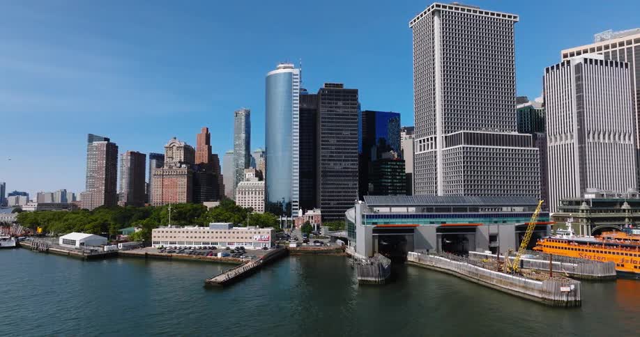 Aerial footage pans left across the Lower Manhattan skyline and waterfront, showing the Staten Island Ferry terminal on a sunny day