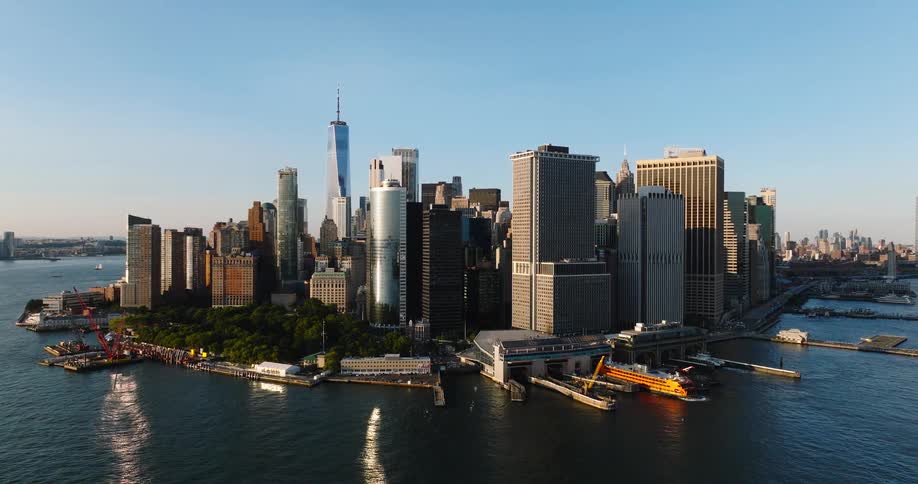 A breathtaking aerial view reveals the iconic Lower Manhattan skyline and the Staten Island Ferry terminal during a sunny golden hour