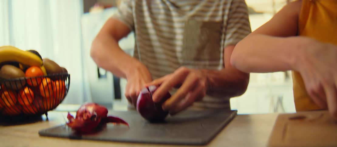 Close-up slow motion shot of a young man carefully slicing a fresh red onion on a cutting board in a brightly lit kitchen