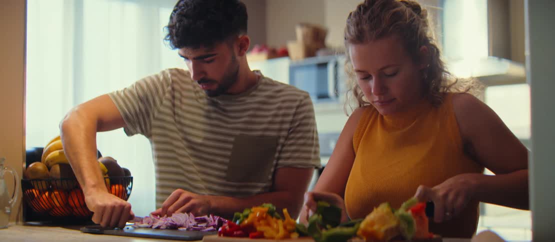 Young man and woman chopping fresh vegetables together in a home kitchen
