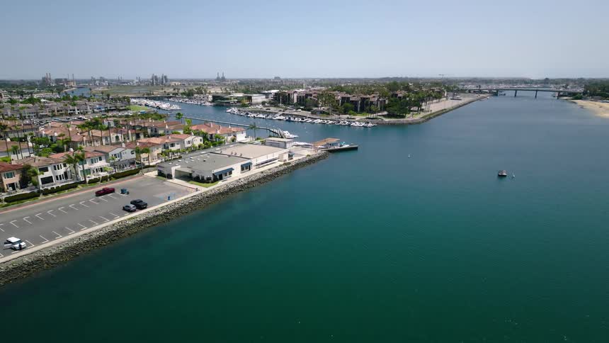 A static aerial view showcases the tranquil waters of a coastal harbor, lined with beautiful waterfront homes and a marina under a clear sunny sky
