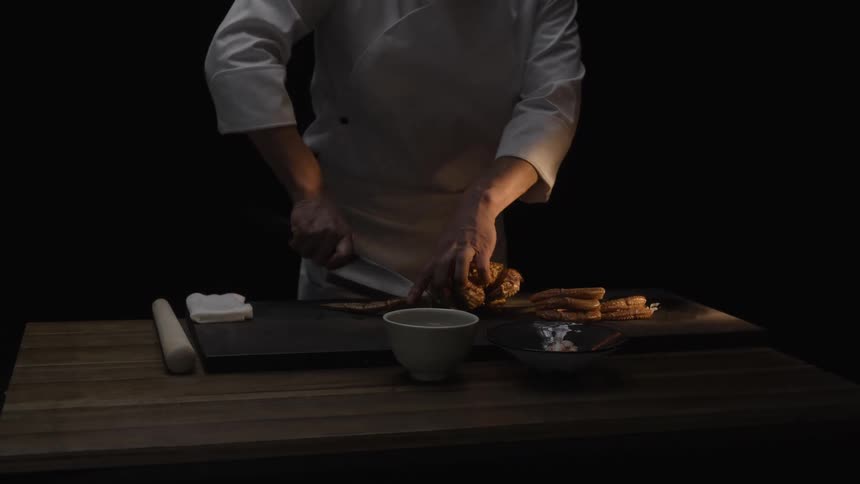In a dramatically lit setting, a skilled chef meticulously prepares fresh snow crab legs with a sharp knife