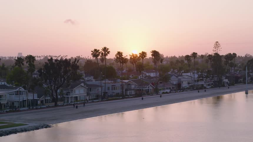 Aerial view of a beautiful sunset over Long Beach, CA with houses and palm trees lining the calm water's edge