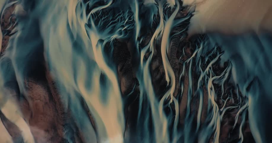 Ethereal top-down aerial view of a braided glacial river flowing through a dark landscape, resembling veins or tree roots