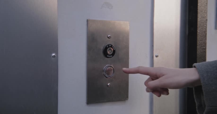 Close-up of a person's finger pressing a vintage metal elevator button