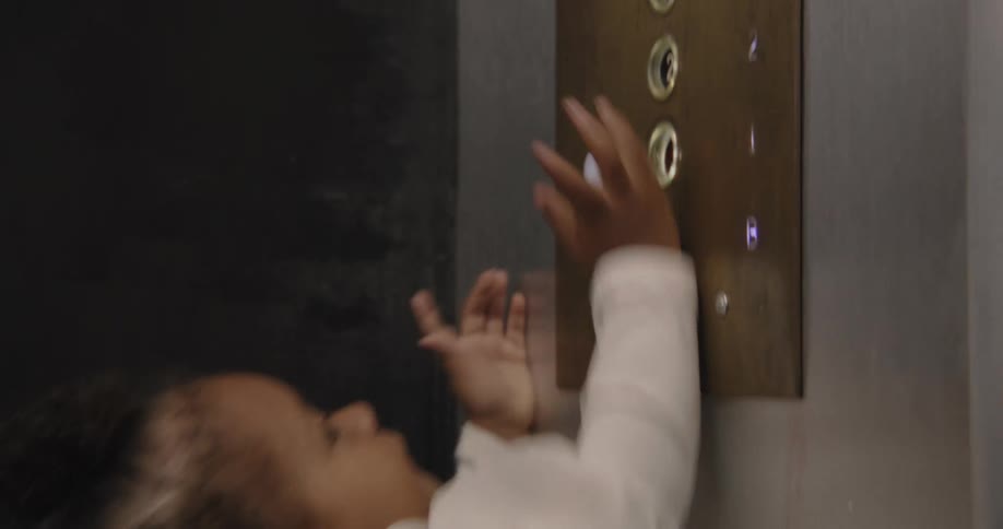 A curious toddler reaches up to press the buttons on an old elevator control panel