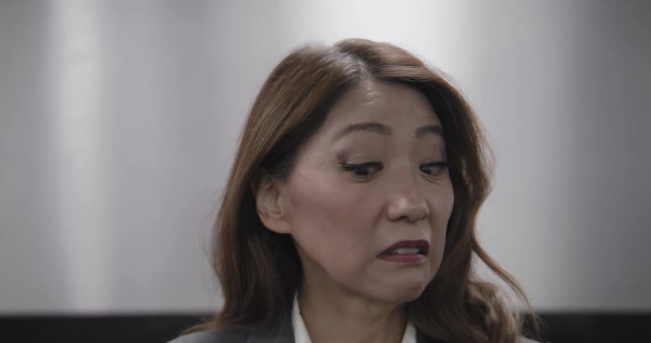 A professional woman looks around with concern and disgust before fainting and falling out of the frame in slow motion