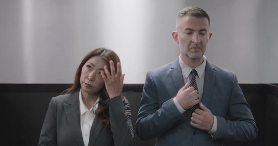 A professional man adjusts his tie and a woman fixes her hair as they compose themselves while riding in an elevator