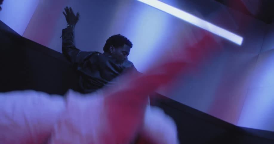 A dynamic Dutch angle shot captures a man and woman performing an expressive dance routine inside a small, neon-lit elevator