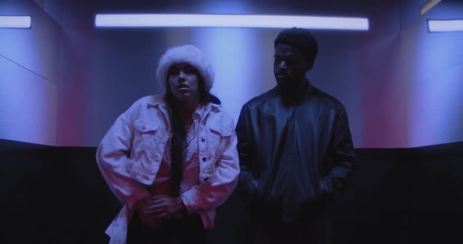 A stylish man and woman start dancing in an elevator after the doors open in a vibrant red hallway
