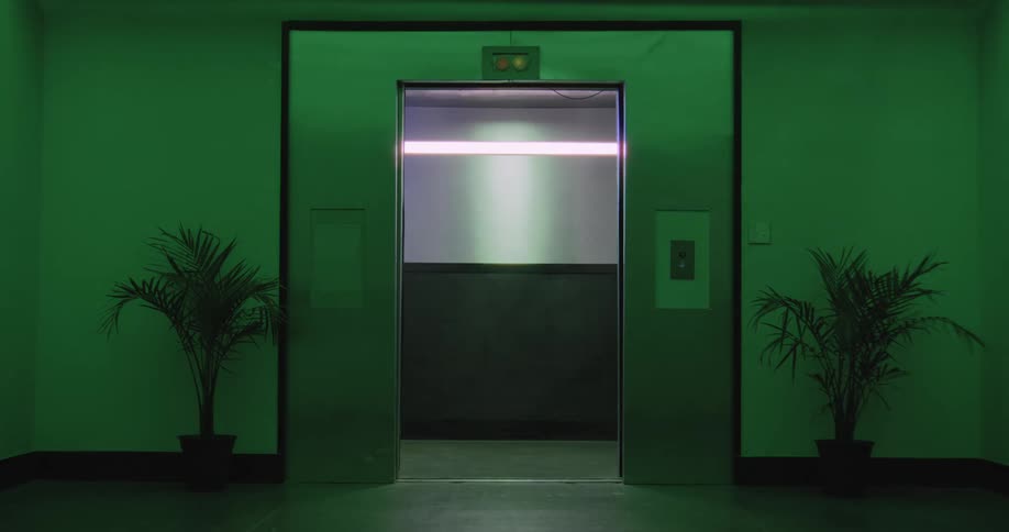 An elevator with stainless steel doors opens in a dark, empty hallway illuminated by a mysterious green light