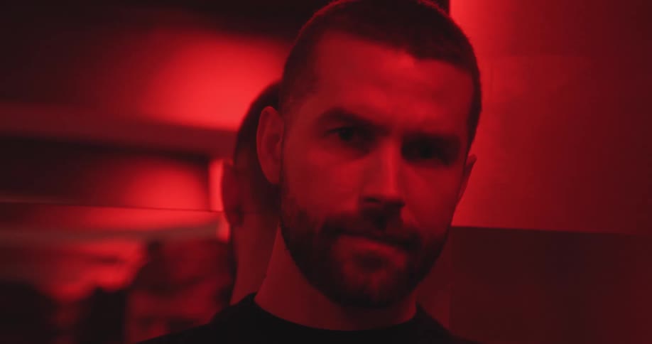 A moody close-up portrait of a serious bearded man looking at the camera in a dark room with dramatic red lighting